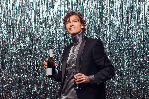 Holidays concept - happy tipsy man with bottle of champagne and wine glass at christmas or new year party on a sparkle background. - Фото, зображення