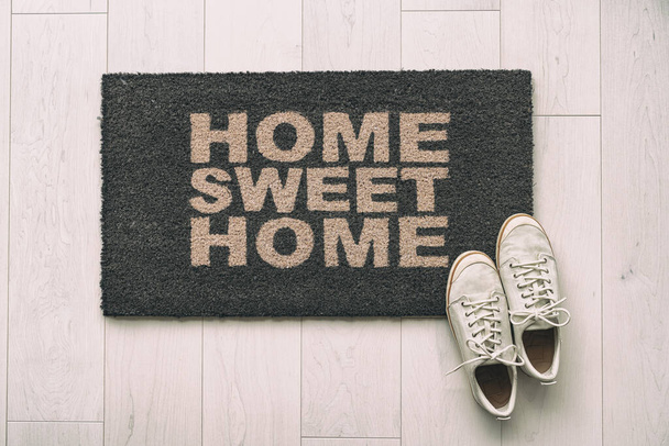 Moving in new condo apartment Home sweet home text doormat at house entrance with womens sneakers of woman that has just arrived. Home background, - Foto, Imagen