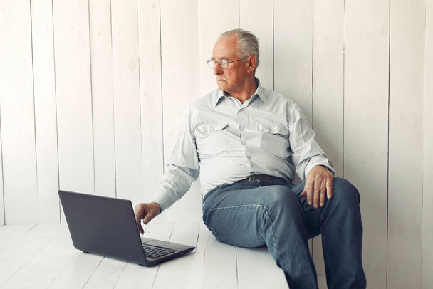 Elegant old man sitting at home and using a laptop - Zdjęcie, obraz