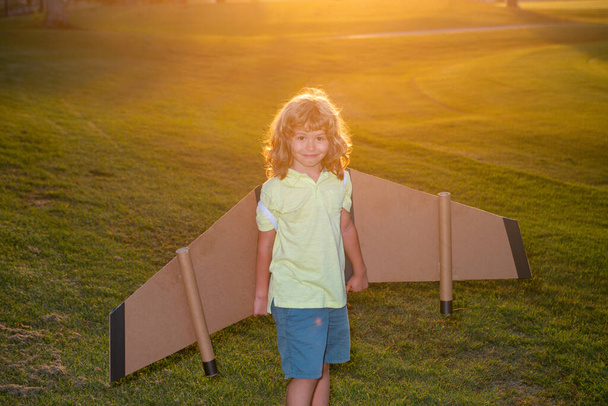 Kid pilot with backpack wings at sunset grass field. Child playing pilot aviator and dreams outdoors in park. - Photo, image