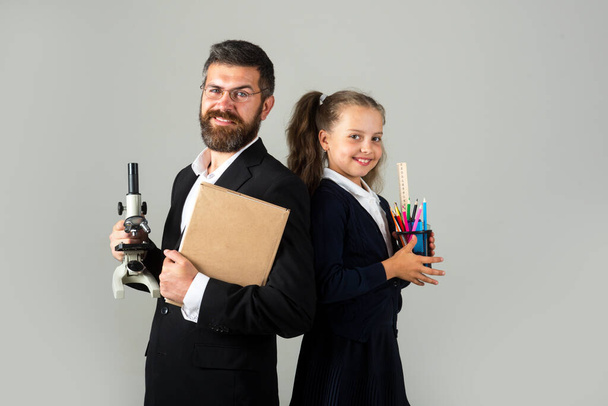 Smiling teacher with excited happy pupil school girl. Portrait of funny school girl and tutor with school supplies. Happy teacher and student girl on gray. Back to school, student girl in uniform. - Foto, Imagem