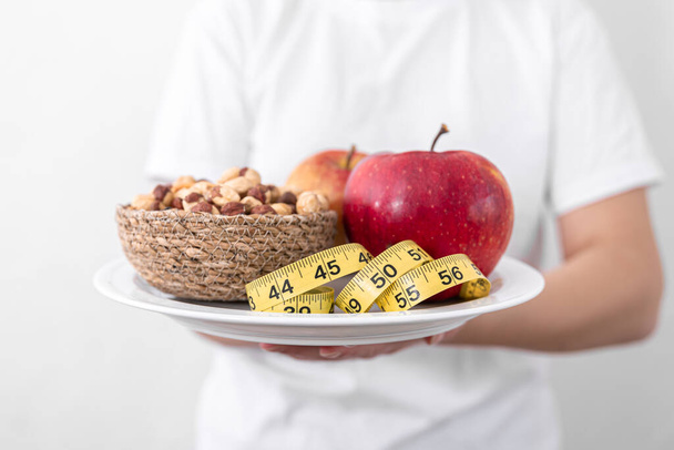 Тарілка з яблуками, горіхами та вимірювальною стрічкою, дієта та концепція здорового харчування
. - Фото, зображення