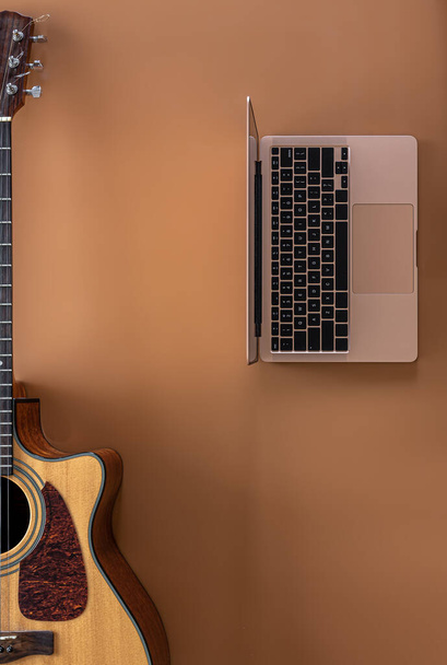 Acoustic guitar and laptop on a brown background, top view, copy space. - Photo, Image