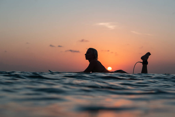 Portrait of surfer girl with beautiful body on surfboard in the ocean at colourful sunset time in Bali - Photo, image