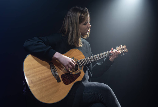 Young woman playing acoustic guitar in a dark room with haze. - Fotoğraf, Görsel