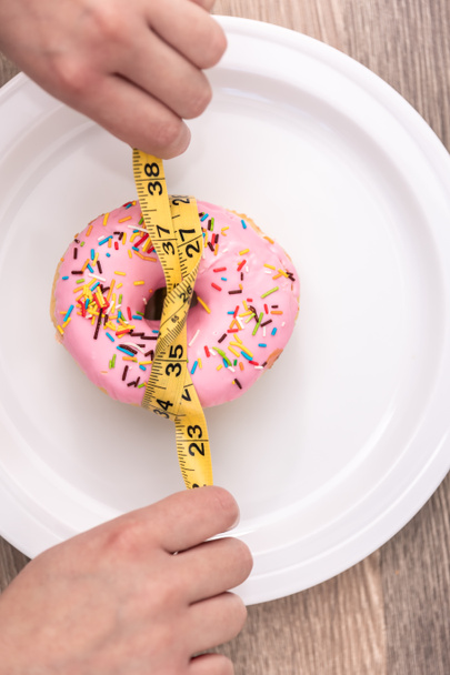 Close up of donut and measuring tape, weight loss and diet concept. - Photo, Image