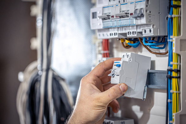 een mannelijke elektricien werkt in een schakelbord met een elektrische aansluitkabel. - Foto, afbeelding