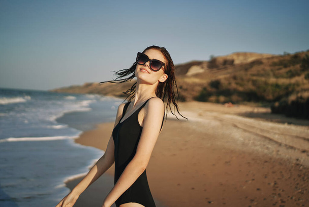 woman walks along the sandy shore in a black swimsuit sun tropics - Foto, imagen