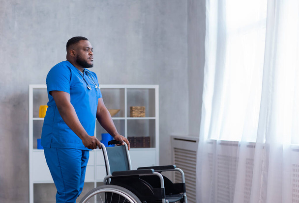 Caregiver and an empty wheelchair. Professional nurse in a nursing home. Assistance, rehabilitation and health care. - Fotó, kép