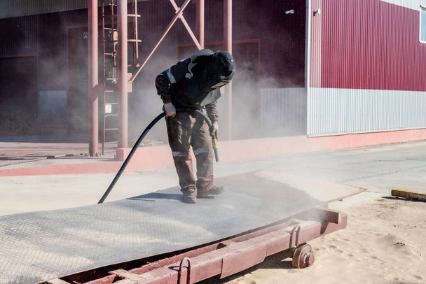 Um trabalhador em um terno especial está jateando metal em um local industrial - Foto, Imagem
