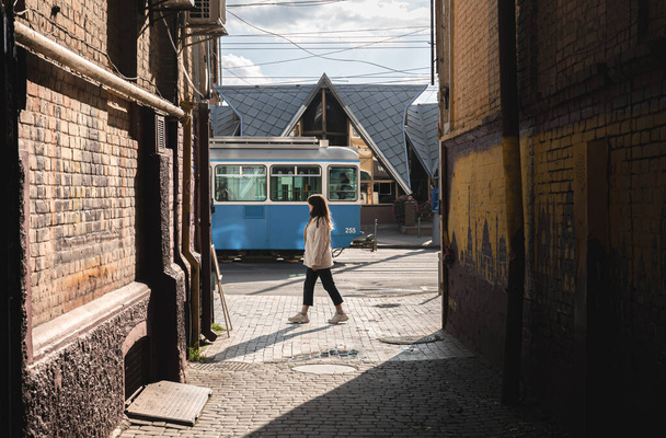 Una donna cammina lungo la strada sullo sfondo di un tram di passaggio. - Foto, immagini