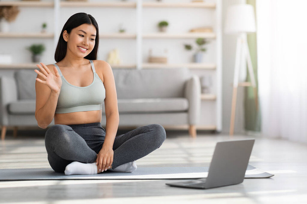 Felice giovane asiatica femminile utilizzando il computer portatile a casa per l'allenamento di fitness online - Foto, immagini