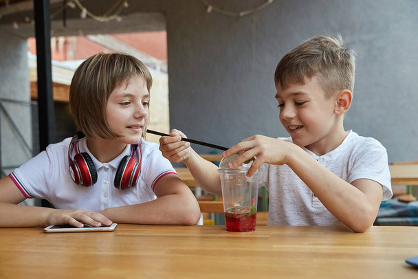 kaukaskie dzieci siedzące w kawiarni, bawiące się jagodami w filiżance lemoniady - Zdjęcie, obraz