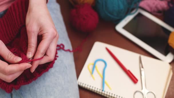 Uma mulher tricota um chapéu de fio de lã e escreve em um caderno. - Filmagem, Vídeo