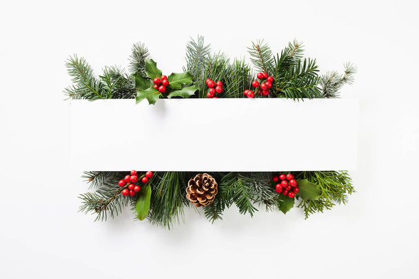 Composition of red holly berries and green fir tree branches on white background. Winter natural decoration. Botanical festive flat lay, top view. - Foto, immagini