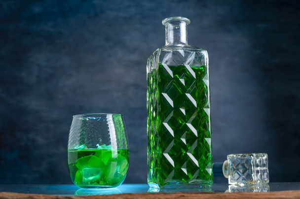 A view of a decanter and a glass with a green drink on the dark background - Fotografie, Obrázek