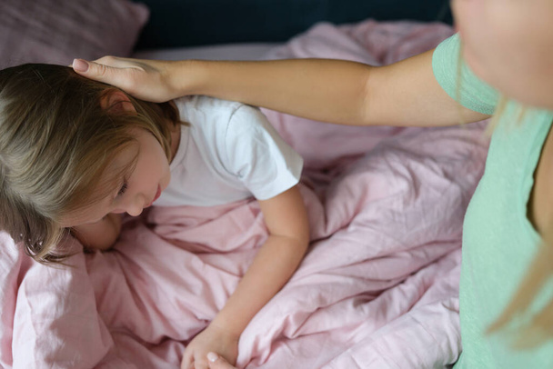 Маленькая девочка грустит на кровати, рядом с мамой - Фото, изображение