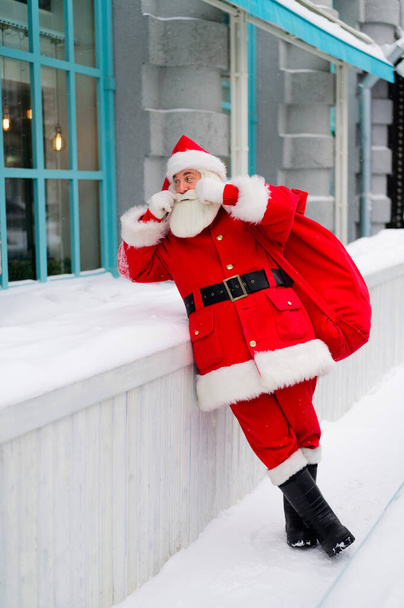 Pensive santa claus is leaning against the facade of a house in winter - Photo, image