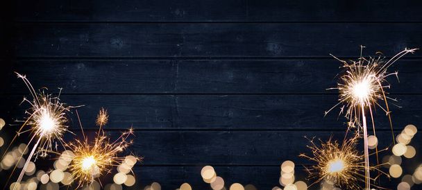 Luces bokeh doradas bengalas y bengalas aisladas en textura de madera de color azul rústico - Fiesta de Nochevieja Silvester Año Nuevo Fiesta de fondo festivo banner tarjeta de felicitación - Foto, imagen