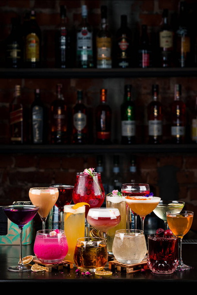 様々なカラフルなカクテルがグラスに入っています。バーで近代的なアルコール飲料。バーカウンターのカクテルをダークバーの背景に垂直にセットし - 写真・画像