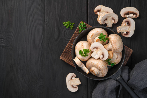 Raw mushrooms in a frying pan on a black background. Top view, copy space. Cooking mushrooms. - Photo, Image