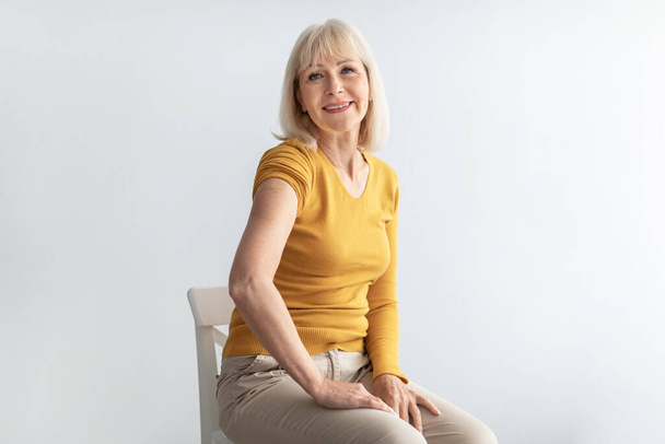 Mujer mayor paciente que muestra brazo vacunado con yeso, fondo gris - Foto, Imagen