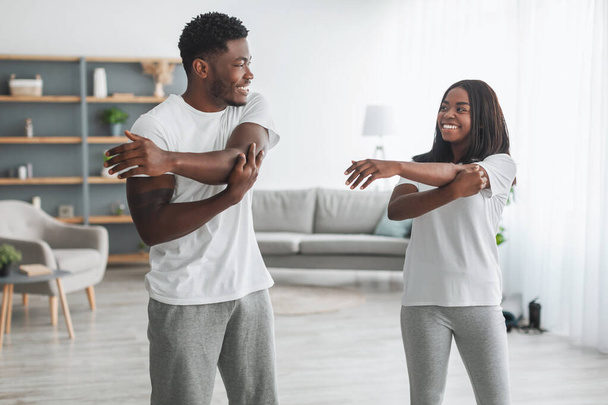 joven negro pareja haciendo brazo estiramiento ejercicio juntos en casa - Foto, Imagen