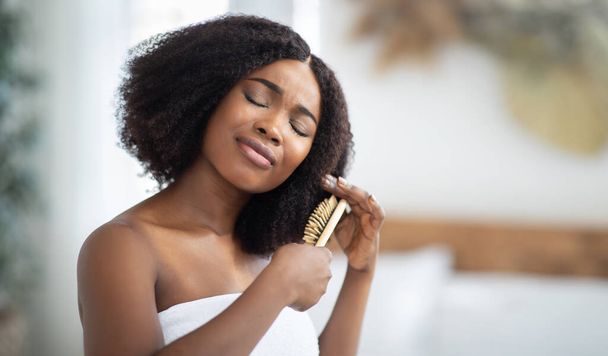 Frustrada jovencita negra que tiene problemas para cepillarse el cabello enredado en casa, pancarta con espacio para copiar - Foto, imagen