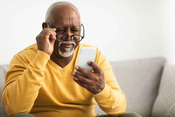 Hombre negro usando Smartphone usando anteojos que tienen mala vista en interiores - Foto, imagen