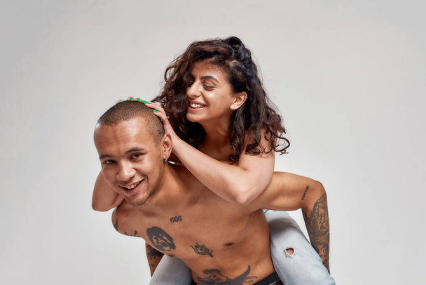 Young couple, tattooed guy and his girlfriend with curly dark hair having fun while posing together isolated over gray background - Photo, Image