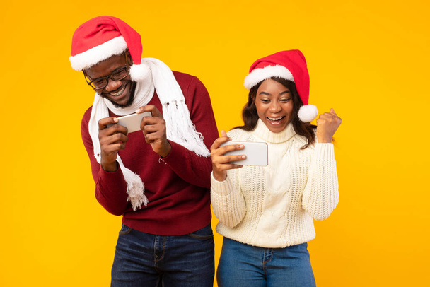 アフリカのカップルは、サンタの帽子をかぶってスマートフォンでゲームをプレイ,スタジオ - 写真・画像