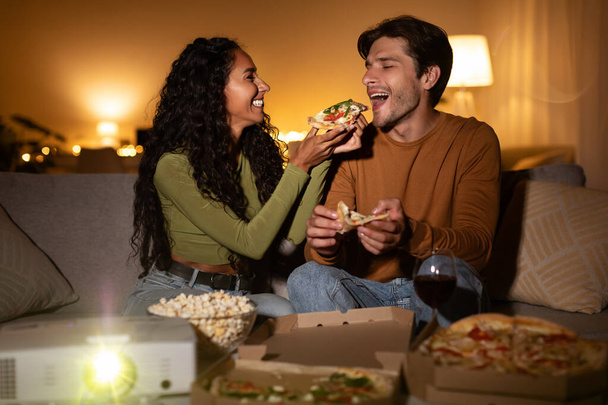 Ζευγάρι τρώει πίτσα ταΐζοντας ο ένας τον άλλο βλέποντας ταινία στο σπίτι - Φωτογραφία, εικόνα