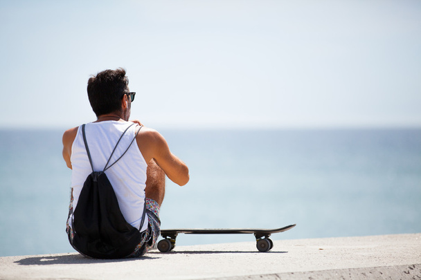 Man sitting at the border of the coast, with a skate.  - Foto, Imagem