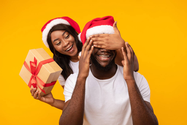 Zwarte vriendin Verrassende vriendje met kerstcadeau over gele achtergrond - Foto, afbeelding