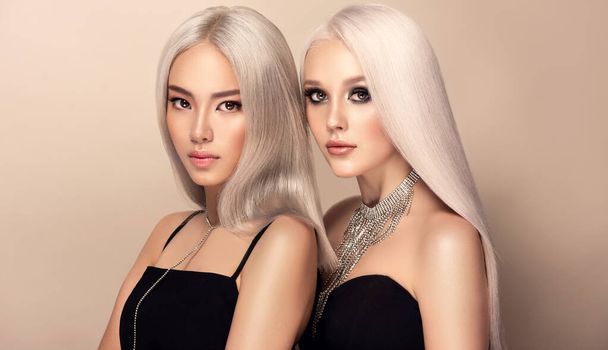 Twee mooie vrouwen in witte jurken met haarkleuring in ultra blond. Stijlvol meisje kapsel krullen gedaan in een schoonheidssalon. Mode, cosmetica en make-up. - Foto, afbeelding
