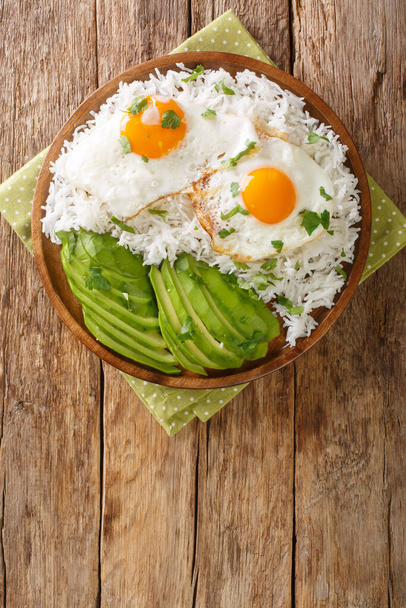 Ekwadorskie proste śniadanie z gotowanego ryżu i smażonych jaj zbliżenie w talerzu na stole. widok pionowy z góry z góry - Zdjęcie, obraz