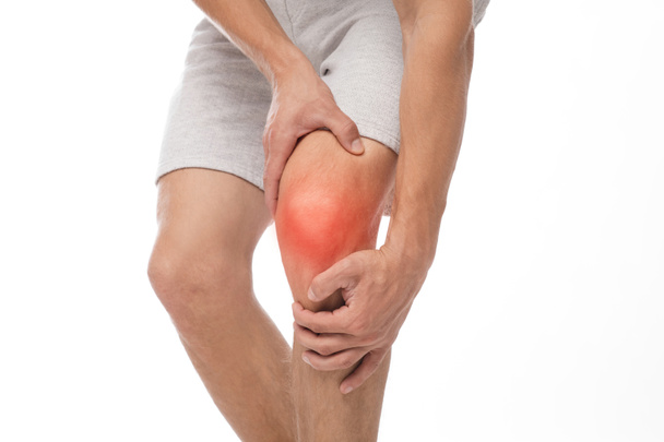 Jeune caucasien méconnaissable souffrant de douleurs au genou, presse la main à la tache douloureuse, inflammation surlignée en rouge - Photo, image