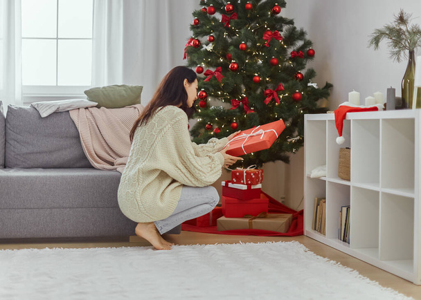 Žena s přítomností v dárkové krabici v blízkosti vánočního stromu doma - Fotografie, Obrázek