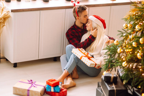 A loving happy young couple enjoying time together near Christmas tree. Romantic day. Winter holidays. - Foto, imagen