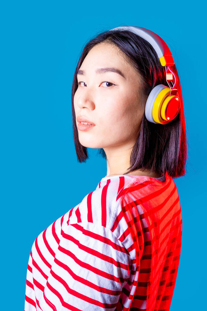 Mujer asiática segura en el interior con auriculares inalámbricos que buscan cámara disfrutando de música en streaming positiva - Foto, imagen