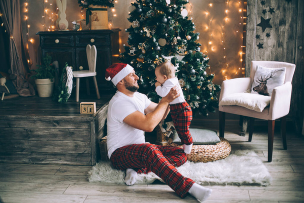 Smiling man holding his baby while playing near Christmas tree - Foto, Imagem