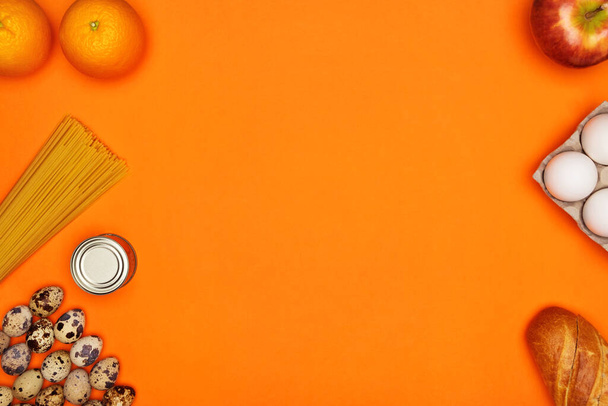 White and quail eggs, spaghetti, bread, oranges, red apple, metal tin on orange background - Photo, Image