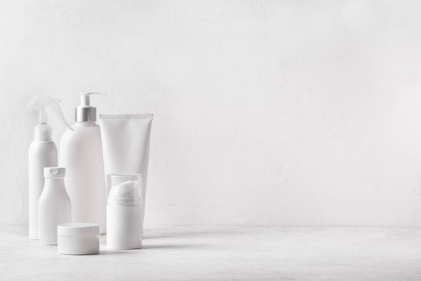 白いバスルームの背景に白い瓶、チューブ、ボトル化粧品容器、コピースペース。バススキンケアアクセサリー。顔と体のケアの概念. - 写真・画像