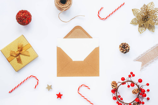 Açık kahverengi zarf, beyaz kart, Noel süslemeleri, baston şekerler ve beyaz masa arkasında hediye kutusu. Üst görünüm, düz görünüm, kopyalama alanı - Fotoğraf, Görsel