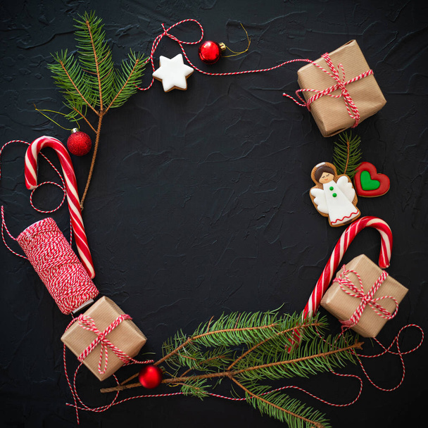 Marco con pan de jengibre, ramas de pino y decoraciones navideñas sobre fondo negro. - Foto, imagen