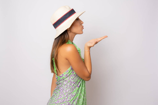 Профиль боковой портрет молодой женщины в летнем наряде и соломенной шляпе, посылающей поцелуй на белом фоне. - Фото, изображение