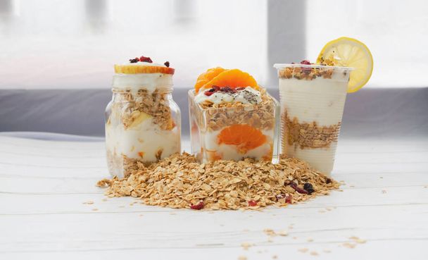 Drie glazen Yoghurt gemengd fruit op de achtergrond, veel cornflakes rond, zelfgemaakte maaltijd, wazig licht rond - Foto, afbeelding
