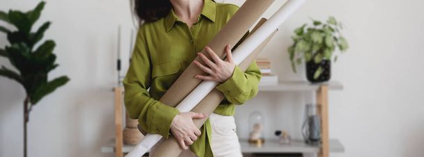 Young woman in green blouse holding rolls of paper blueprints, architecture design and engineering concept. - Φωτογραφία, εικόνα