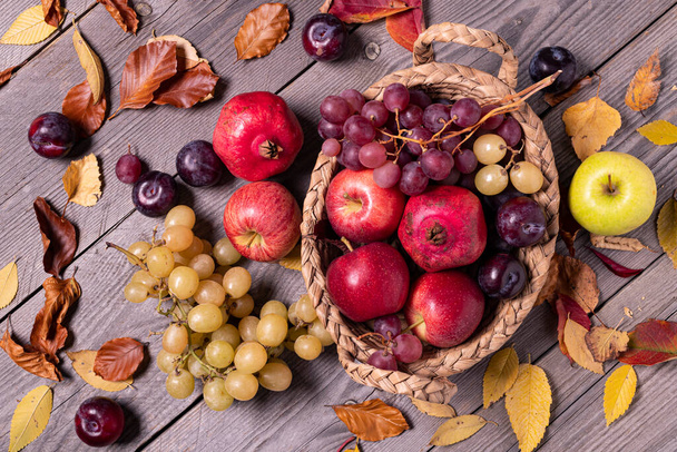 on a rustic wooden background a harvest of seasonal fruit and autumn colored dry leaves. - Fotoğraf, Görsel