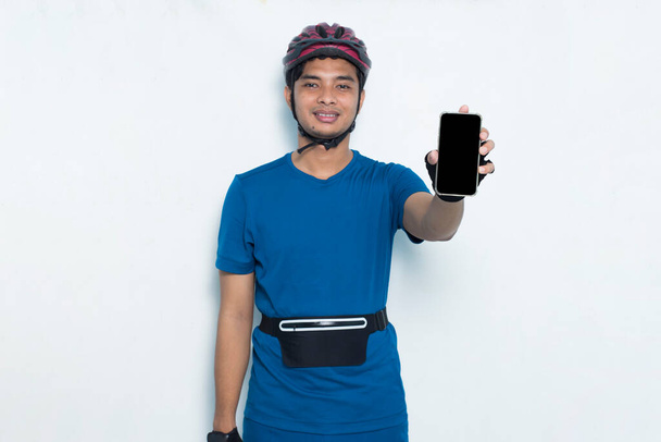 młody Azjata człowiek rowerzysta demonstrujące telefon komórkowy odizolowany na białym tle - Zdjęcie, obraz